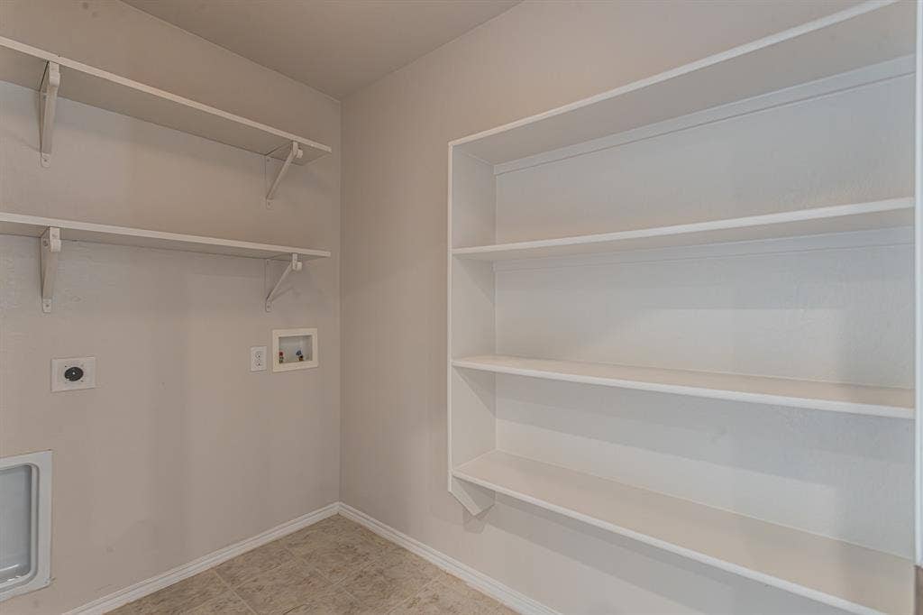 Dedicated utility space featuring extensive built-in shelving, durable tile flooring, and essential appliance hookups