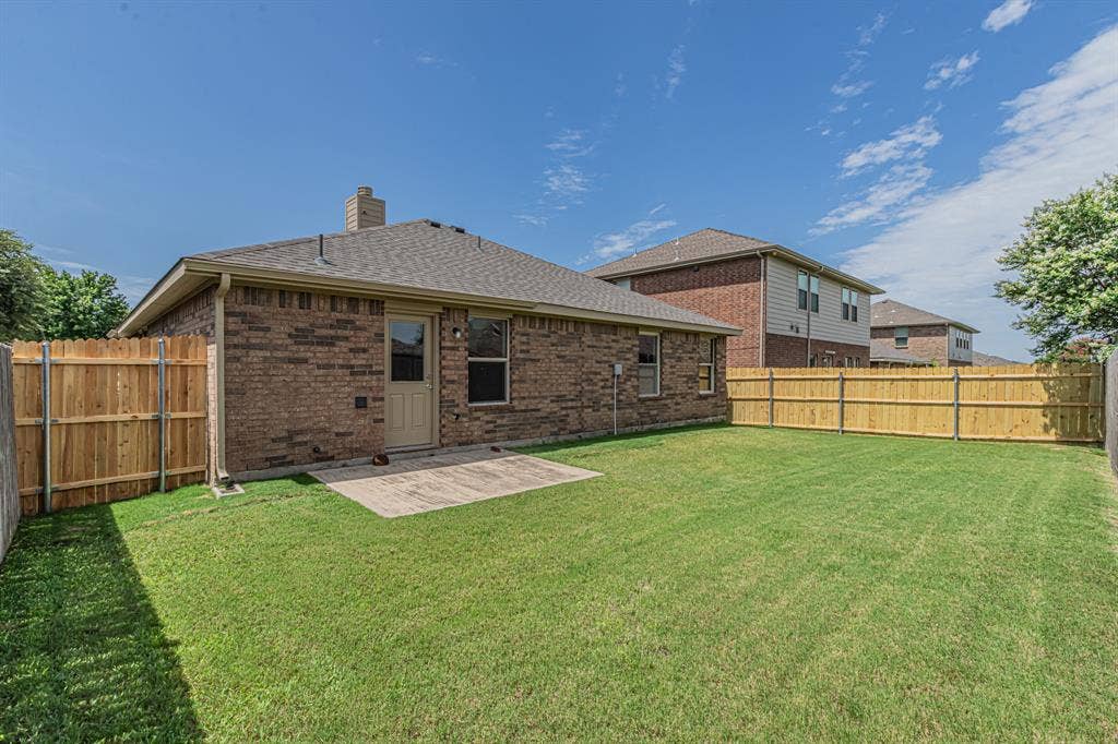 Expansive green lawn with a durable wood privacy fence, a concrete patio, and a brick exterior
