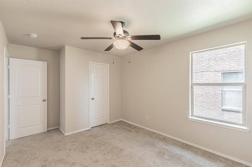 Carpeted room featuring a ceiling fan with integrated lighting, a large window, and two paneled doors