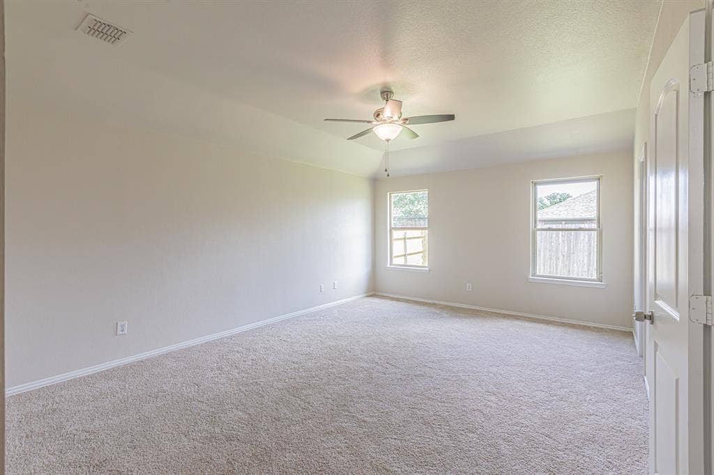 Spacious room featuring neutral carpeting, a ceiling fan with integrated lighting, two windows, and a tray ceiling