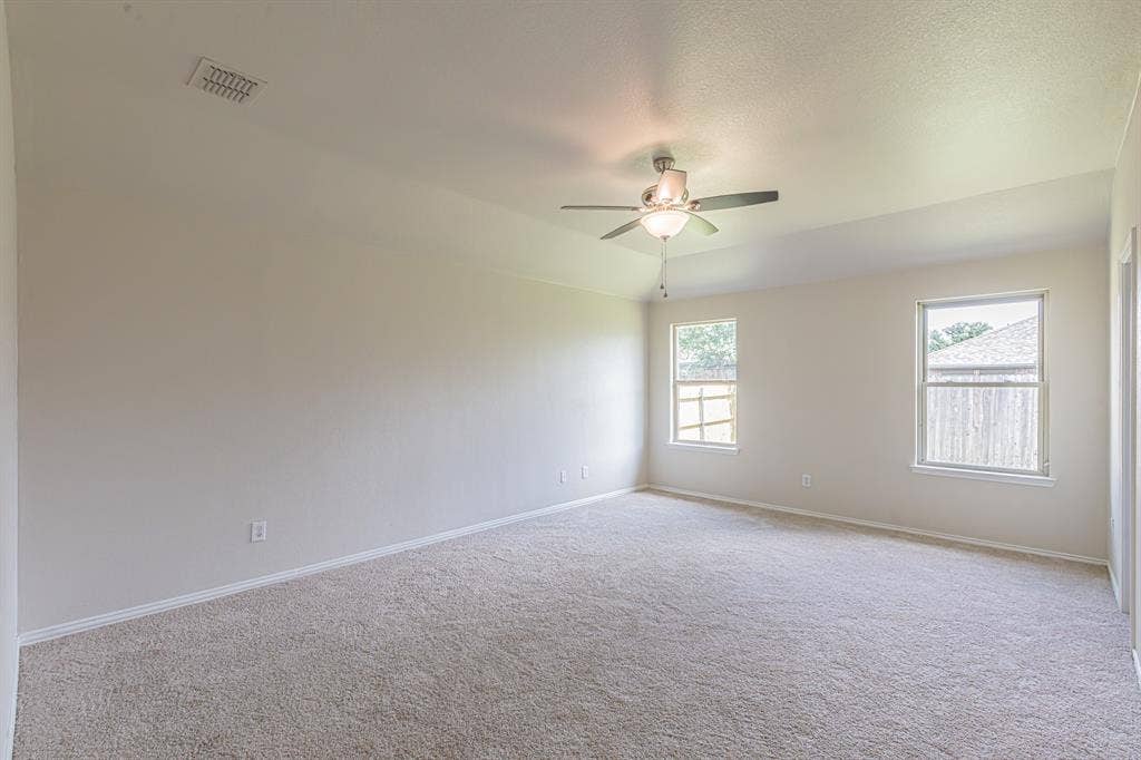 Spacious room featuring neutral carpeting, light-toned walls, and a tray ceiling with a flush-mount ceiling fan