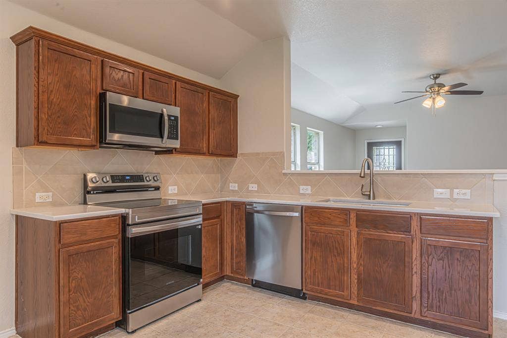 Kitchen featuring wood cabinetry, stainless steel appliances including an oven range and microwave, light-toned countertops, and a tiled backsplash