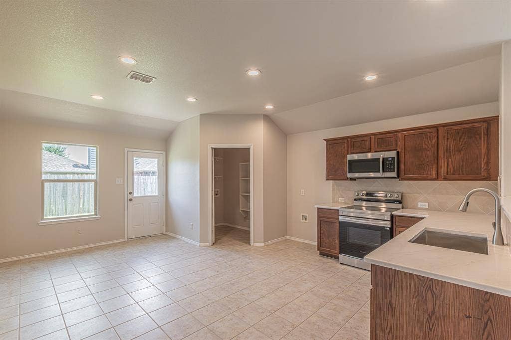Kitchen area with tile flooring, wood-finish cabinetry, stainless steel appliances, and light-toned countertops