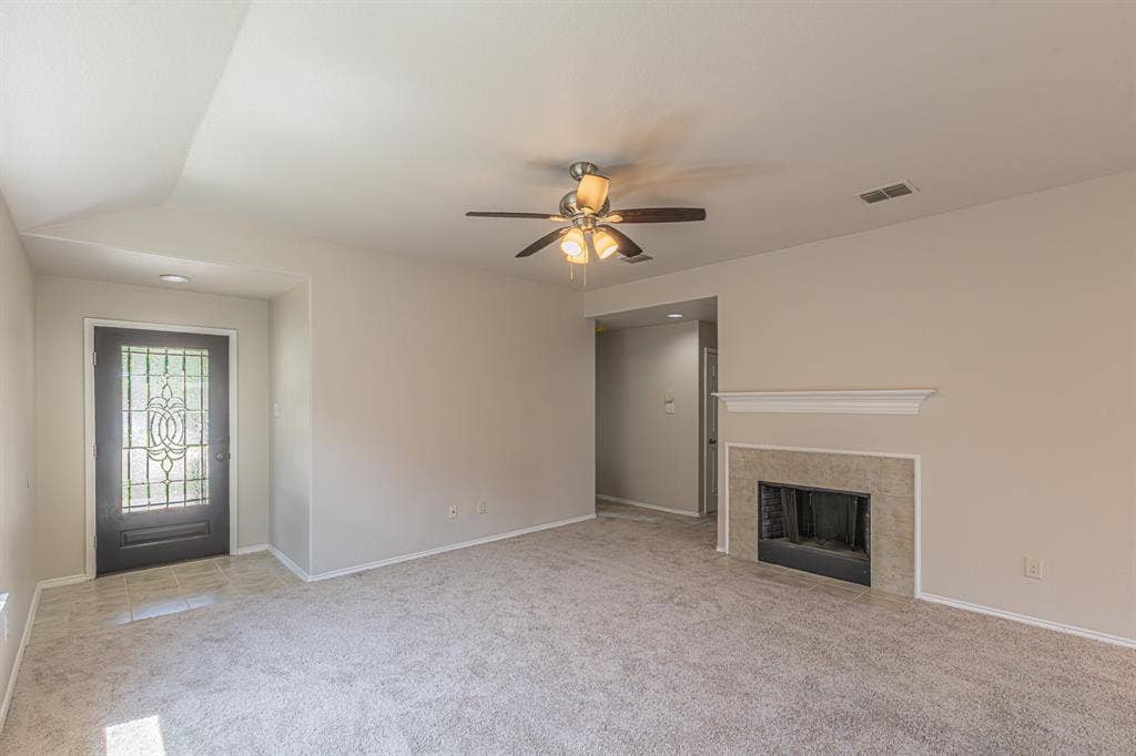 Spacious living area featuring a tile-surround fireplace with a classic mantel, ceiling fan, and carpet flooring