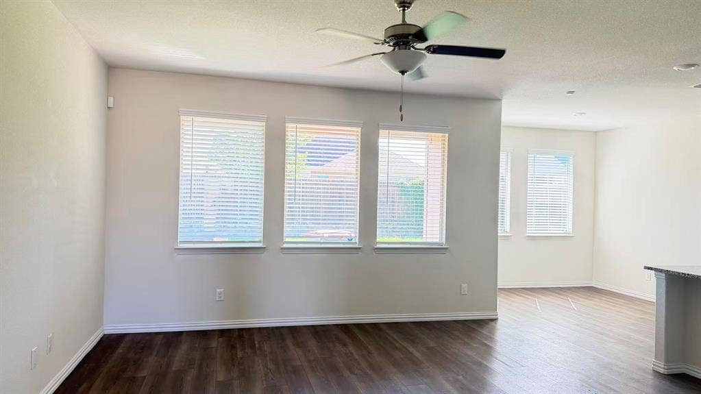 Wood-finish flooring, neutral wall tones, multi-window configuration with horizontal blinds, and a ceiling-mounted light fixture with fan