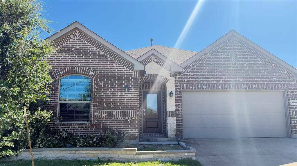Brick and stone facade featuring an arched window, decorative gabled rooflines, and an attached two-car garage