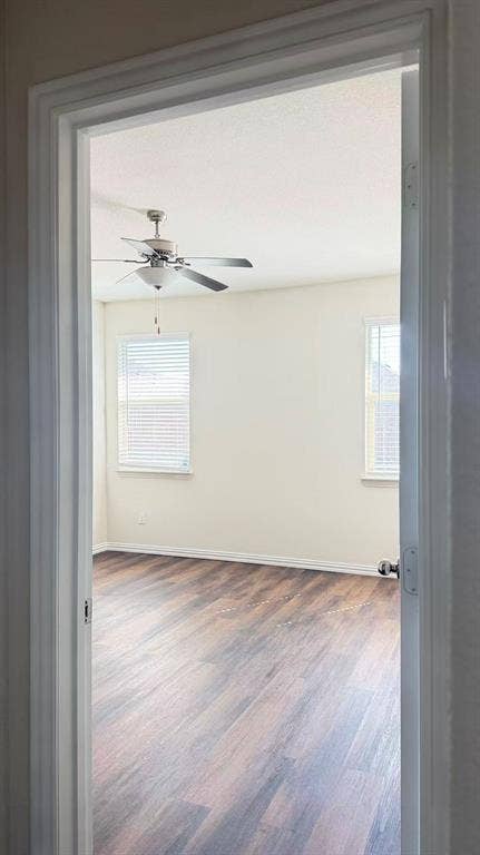Room featuring wood-finish flooring, dual windows with horizontal blinds, and a multi-blade ceiling fan