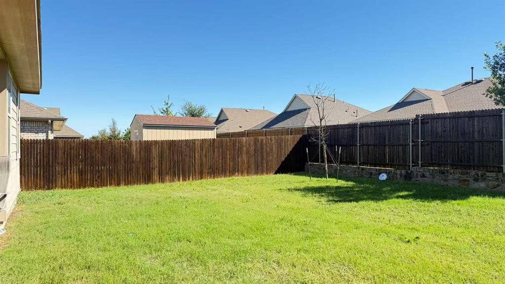 Backyard featuring a grass lawn, stained wood privacy fencing, and stone retaining wall