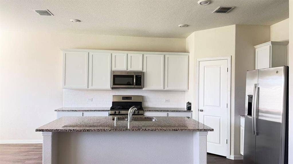 Kitchen featuring white shaker-style cabinetry, stone-finish countertops, stainless steel appliances, a center island with an integrated sink, and subway tile backsplash