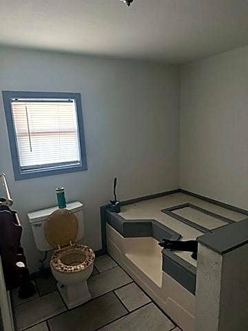 304 11th Street, Abernathy, TX 79311 Bathroom featuring a built-in step-up soaking tub with tile surround, a window with integrated blinds, and tile flooring