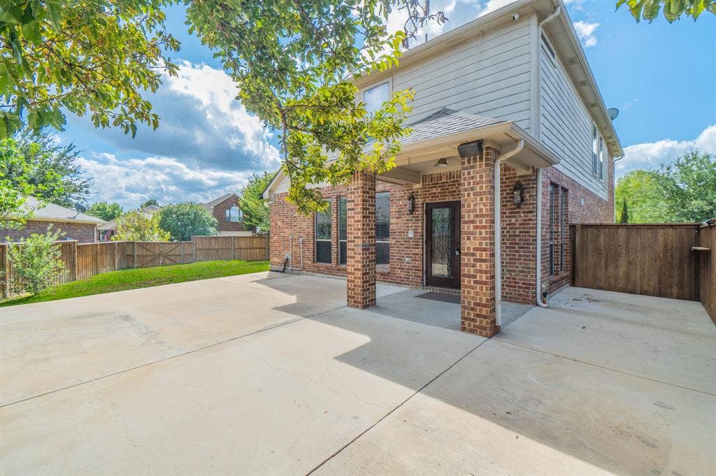 Rear exterior featuring a brick and horizontal siding facade, a covered patio with masonry pillars, and a concrete patio surface enclosed by a wood privacy fence