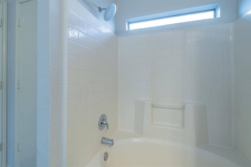Shower and soaking tub combination featuring white wall tiling, a built-in recessed shelf, polished chrome fixtures, and a horizontal clerestory window