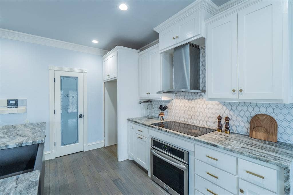 Kitchen featuring custom white cabinetry, stone-surface countertops, geometric patterned tile backsplash, stainless steel appliances, and wood-finish flooring