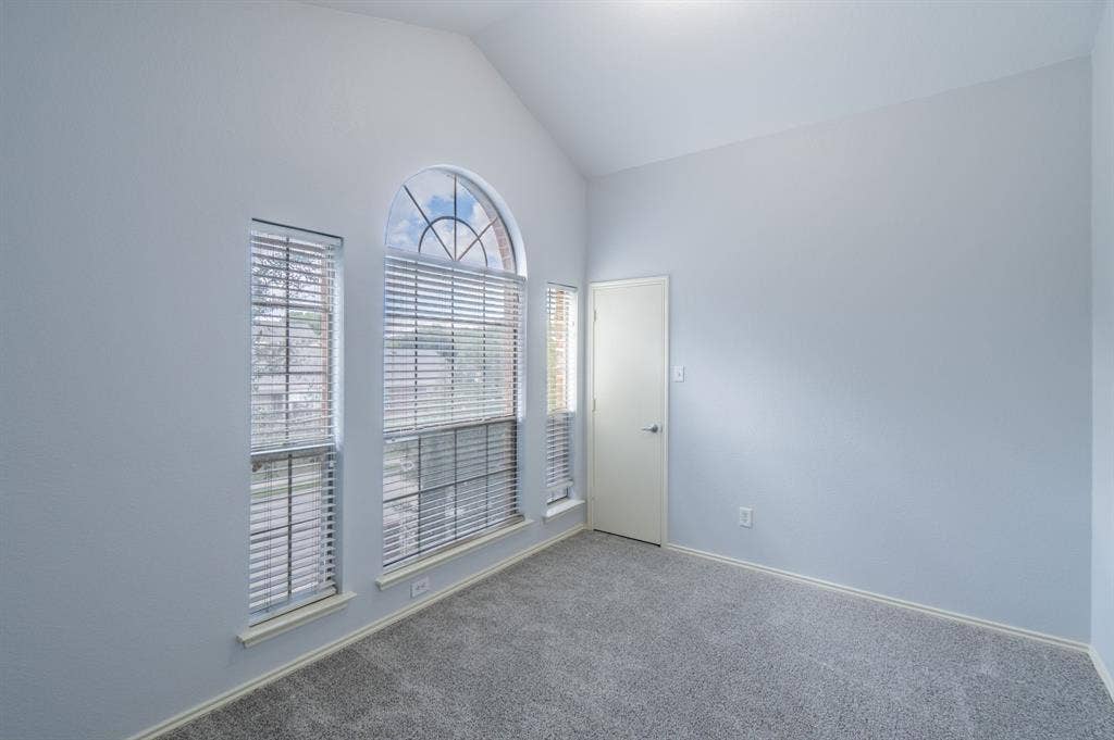 Vaulted ceiling, arched window with fanlight, and neutral wall-to-wall carpeting