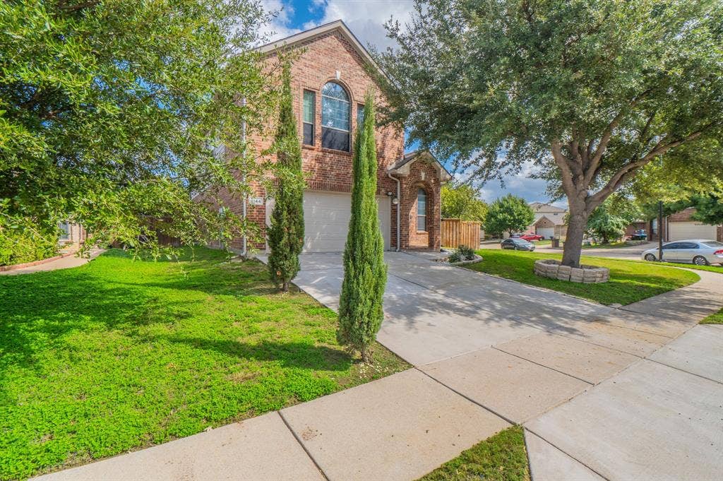 Two-story brick exterior featuring an arched window, attached garage, concrete driveway, and mature landscaping