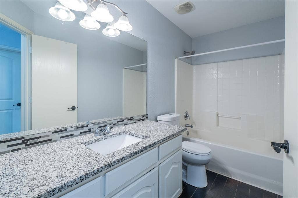 Bathroom featuring a stone-patterned countertop, tile backsplash, undermount sink, multi-light vanity fixture, and a tub-shower combination