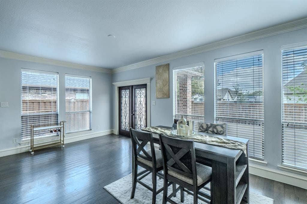 Dark wood-finish flooring, multiple large windows with horizontal blinds, and a double-entry door featuring decorative iron scrollwork inserts
