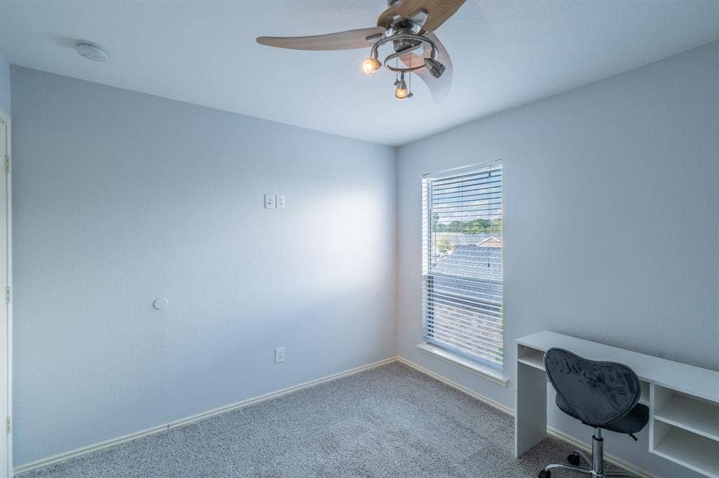 Neutral interior featuring wall-to-wall carpeting, a multi-blade ceiling fan with integrated lighting, and a single-hung window with horizontal blinds