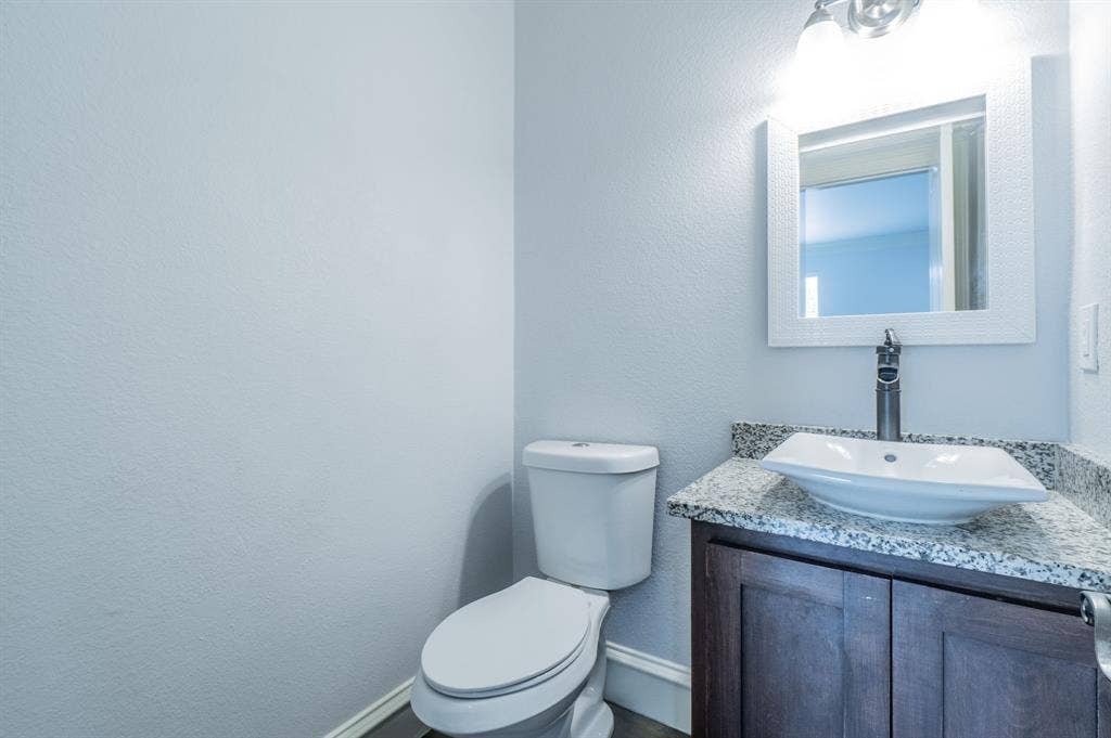 Powder room featuring a dark wood-finish vanity with a stone-finish countertop, white vessel sink, tall faucet, and a wall-mounted framed mirror