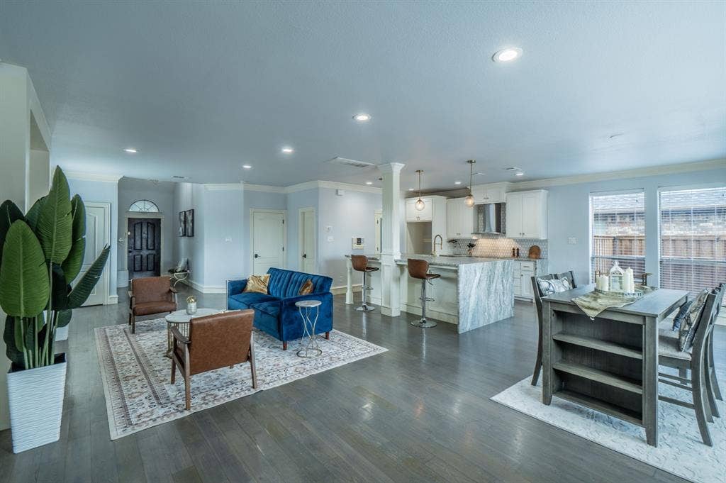 Open-concept floor plan featuring wood-finish flooring, recessed lighting, kitchen island with stone-finish waterfall countertop, and shaker-style cabinetry
