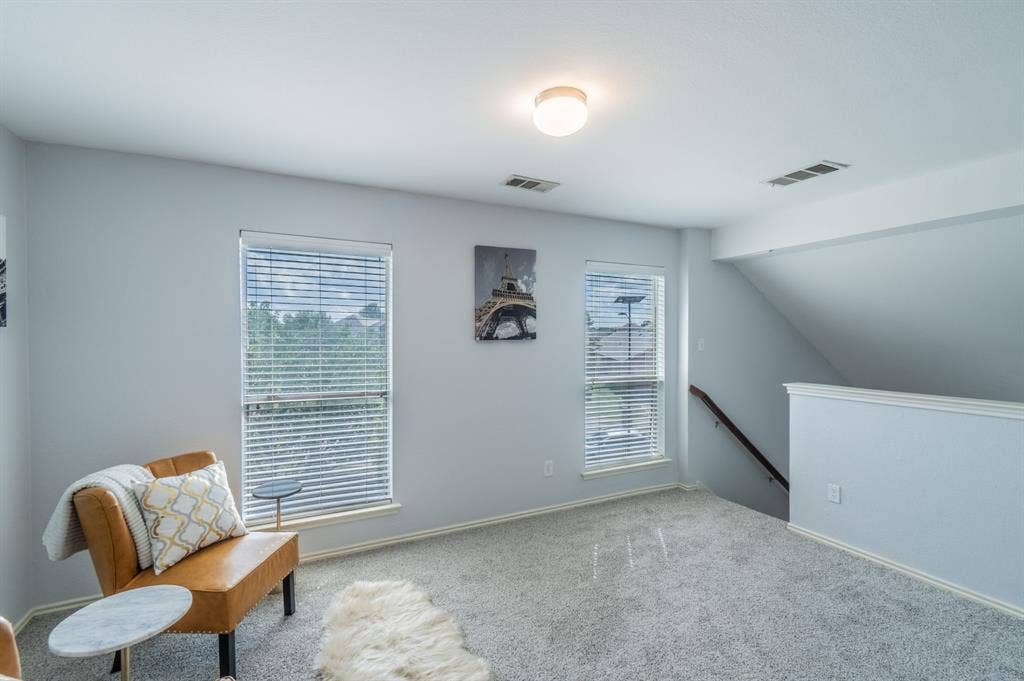 Neutral interior space featuring carpeted flooring, dual windows with fitted blinds, a flush-mount ceiling light fixture, and a stairway with a wooden handrail