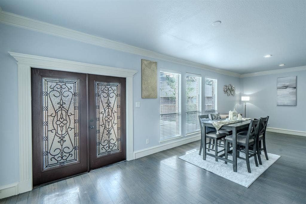 Double entry doors featuring decorative ironwork and glass inserts, wood-finish flooring, crown molding, and a series of windows with horizontal blinds
