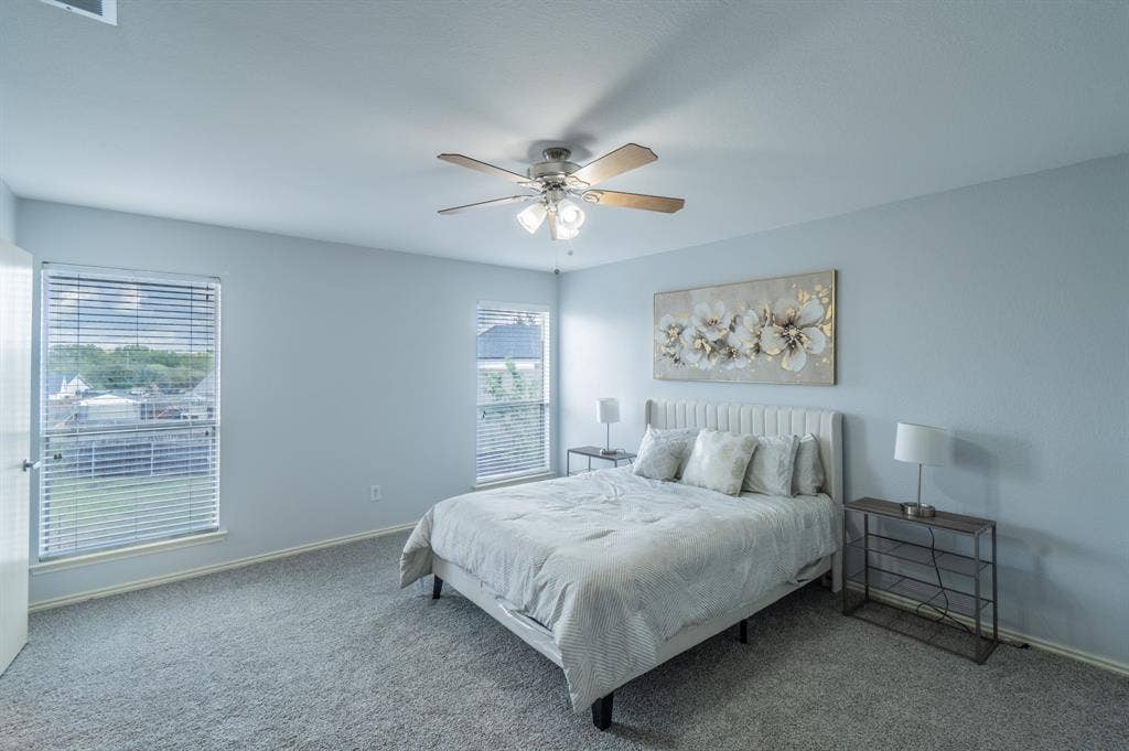 Neutral-toned carpeting, dual windows with horizontal blinds, and a central ceiling fan with multi-light fixture