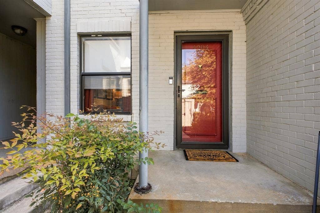4904 Lahoma Street, #4904, Dallas, TX 75235 Painted white brick exterior featuring a red entry door, storm door, single-hung window, and a concrete porch