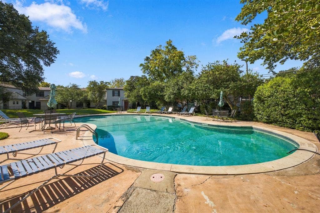4904 Lahoma Street, #4904, Dallas, TX 75235 Curved in-ground swimming pool with a concrete pool deck, mature landscaping, and shaded lawn area