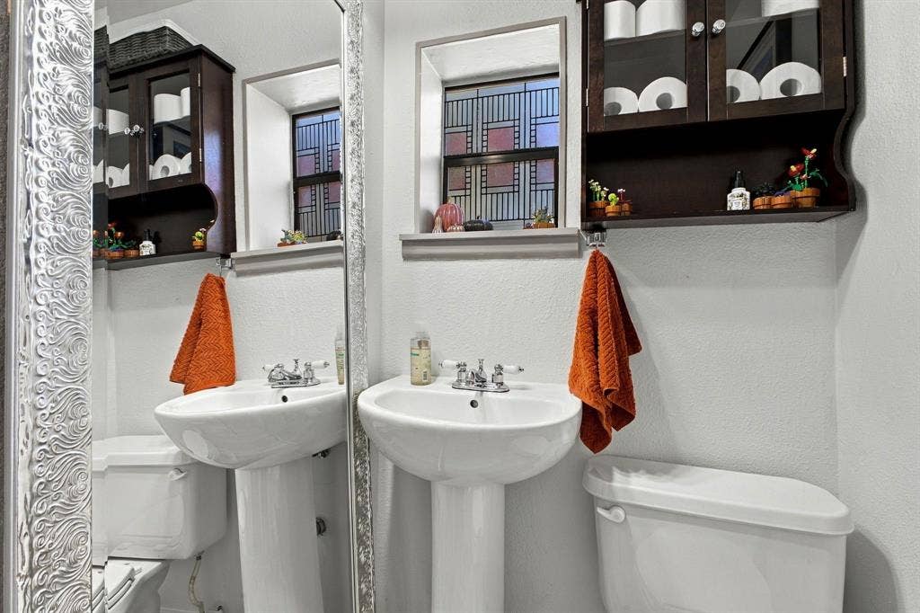 4904 Lahoma Street, #4904, Dallas, TX 75235 Dual pedestal sinks with chrome-finish faucets, wall-mounted dark wood cabinetry with glass-paneled doors, and windows with decorative geometric grids