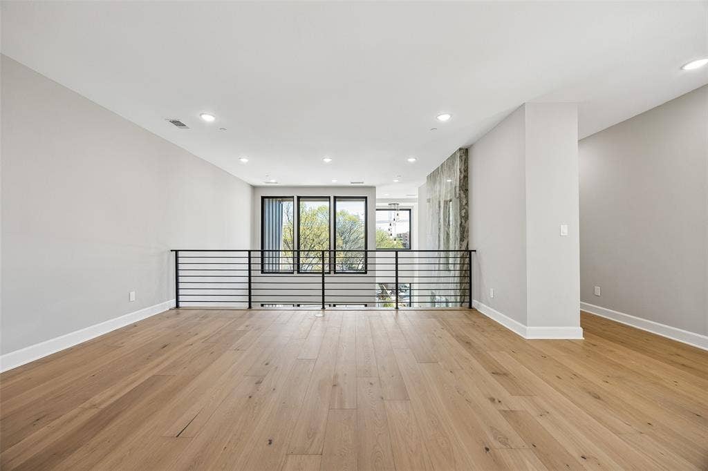 Open-concept space featuring light-toned wood-finish flooring, recessed lighting, matte black horizontal railing, and large windows with black frames