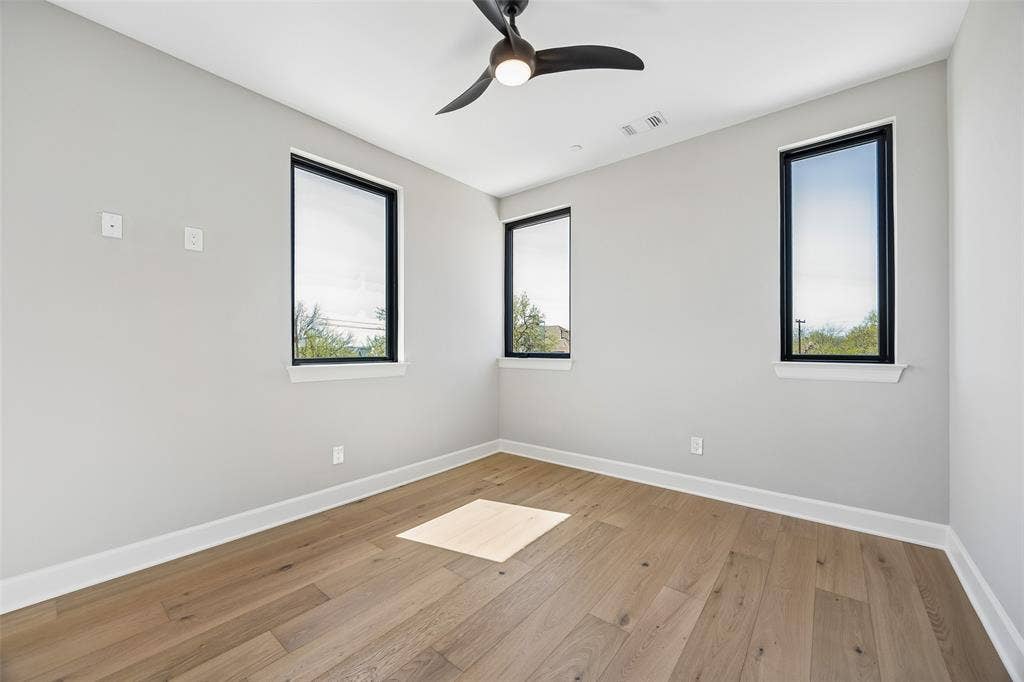 Room featuring wood-finish flooring, three black-framed windows, and a ceiling-mounted light fixture with a fan