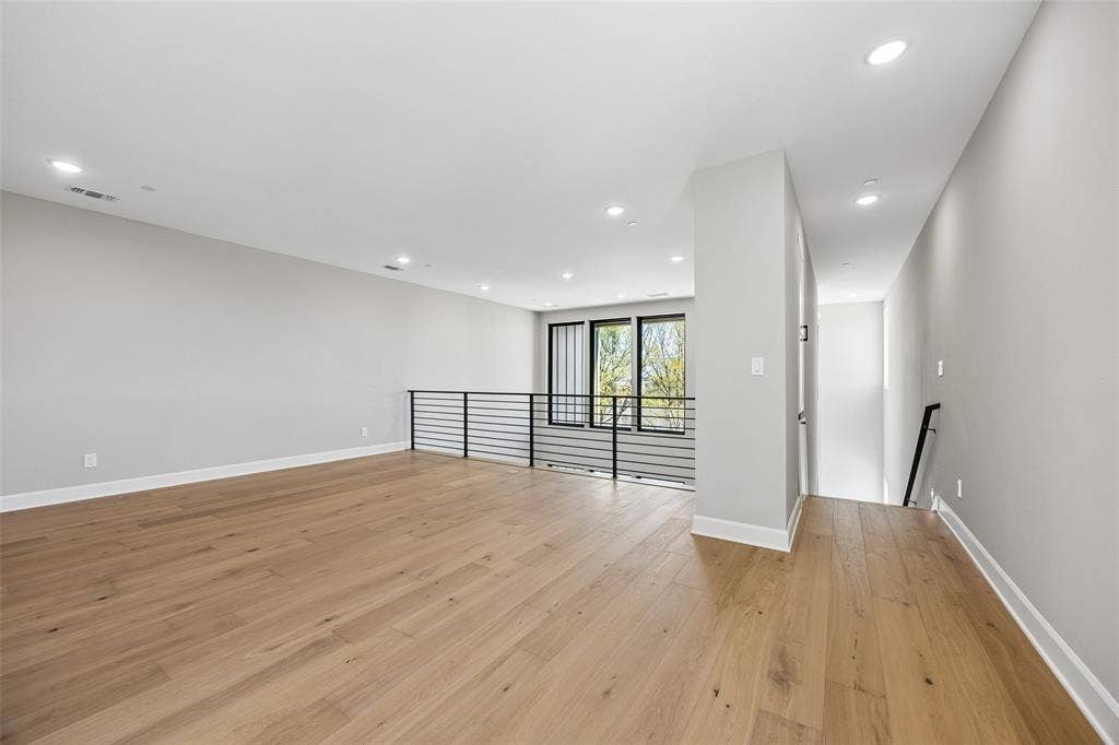 Open-concept area featuring light wood-finish flooring, recessed lighting, neutral wall paint, and a metal horizontal-bar railing