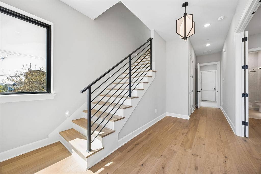 Staircase featuring wood-finish treads and a matte black metal railing, wide-plank wood-finish flooring, geometric pendant lighting, and large rectangular window with a black frame