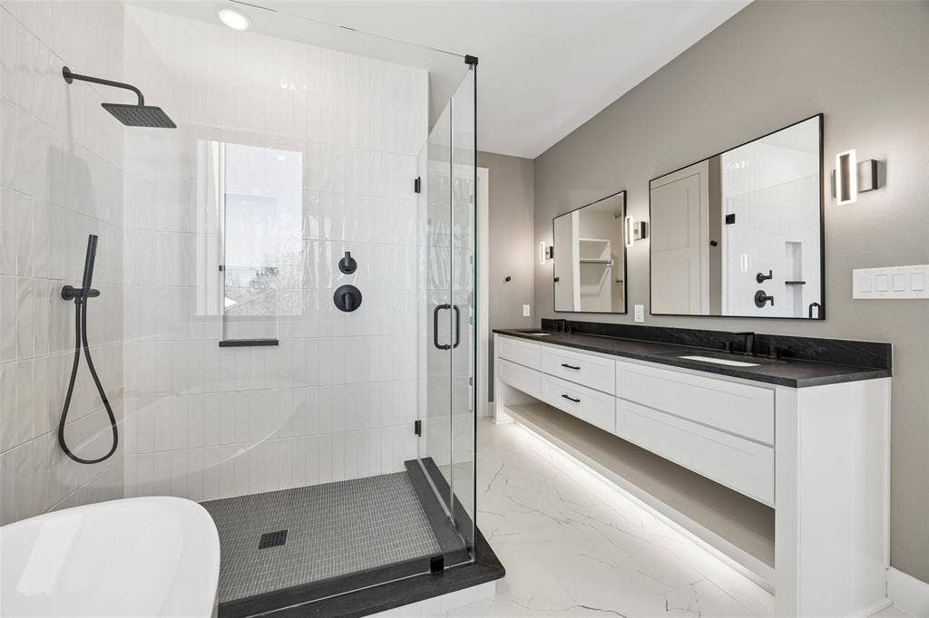 Floating double vanity with a dark countertop and integrated lighting, walk-in shower with a glass enclosure, matte black fixtures, and patterned tile flooring