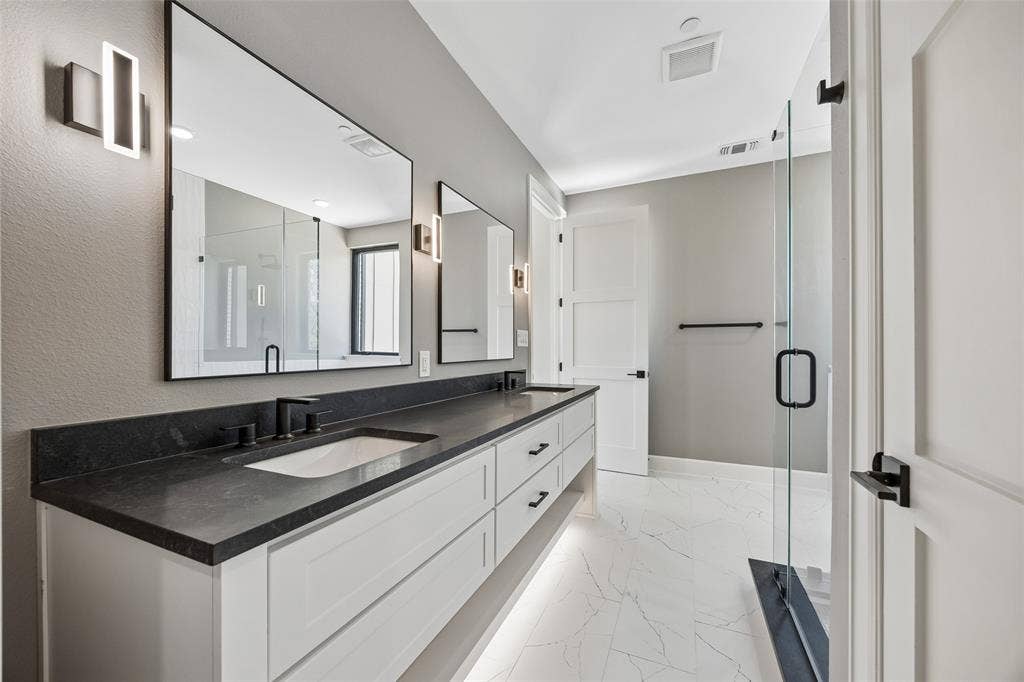 Dual vanity featuring white cabinetry, dark stone countertops, undermount sinks, and wall-mounted linear lighting