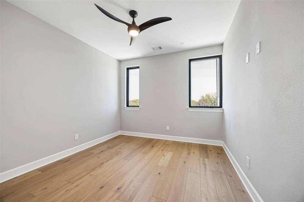 Room featuring light wood-finish flooring, matte black window frames, and a contemporary ceiling fan with integrated lighting