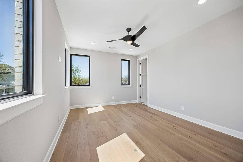 Neutral-toned room featuring wide-plank wood-finish flooring, recessed lighting, matte black ceiling fan, and large windows with black frames
