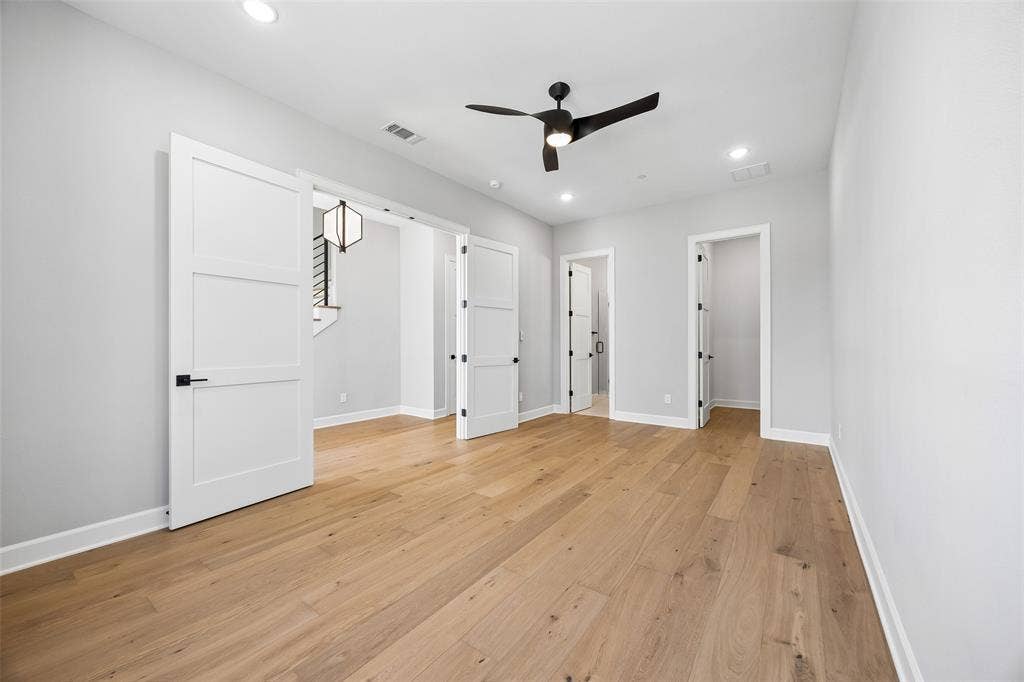 Wood-finish flooring, recessed lighting, three-panel shaker-style interior doors with matte black hardware, and a modern ceiling fan