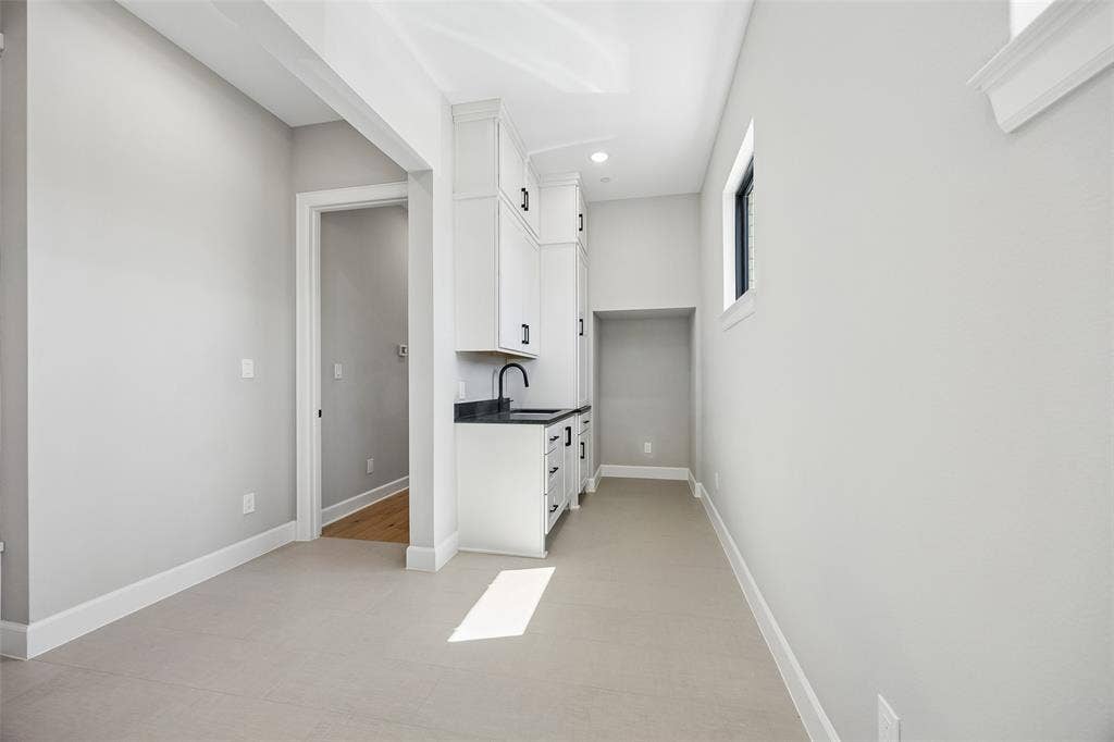 Built-in cabinetry with white finish, dark stone-style countertops, matte black faucet, and light tile flooring