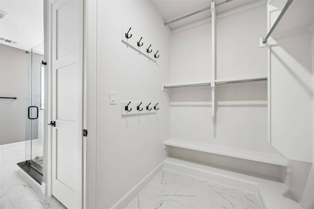 Walk-in closet featuring white built-in shelving, dual-tier hanging rods, two wall-mounted matte black hook racks, and large-format tile flooring with a veined pattern