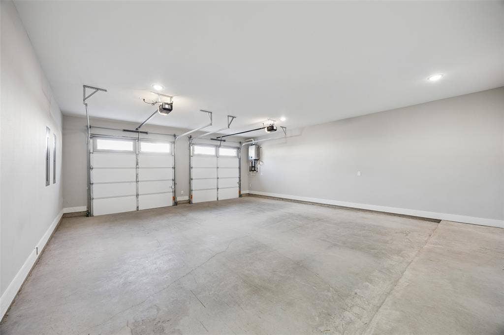 Three-car garage featuring finished walls, concrete flooring, dual automatic door openers, and a wall-mounted tankless water heater