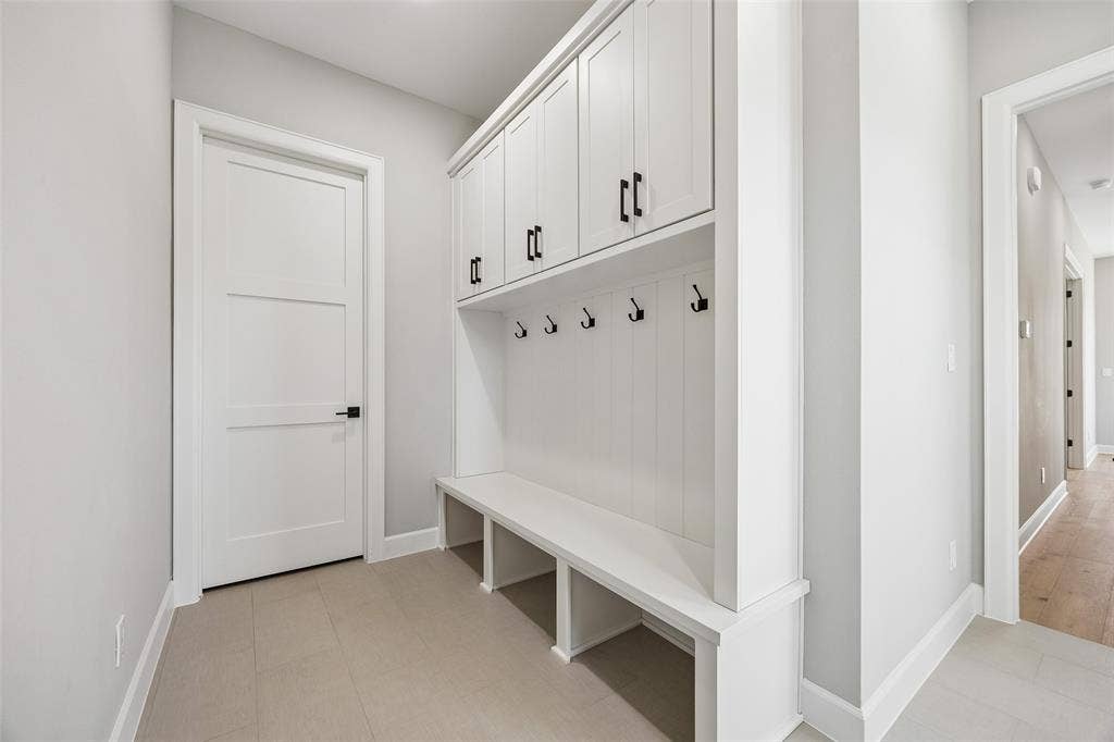 Custom built-in mudroom storage featuring white shaker-style cabinetry, open lower cubbies, a bench seat, and matte black hardware