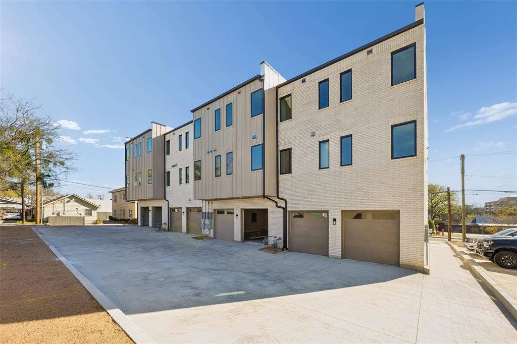 Modern multi-level exterior featuring light brick masonry, vertical metal panel siding, a flat roofline, and attached private garages