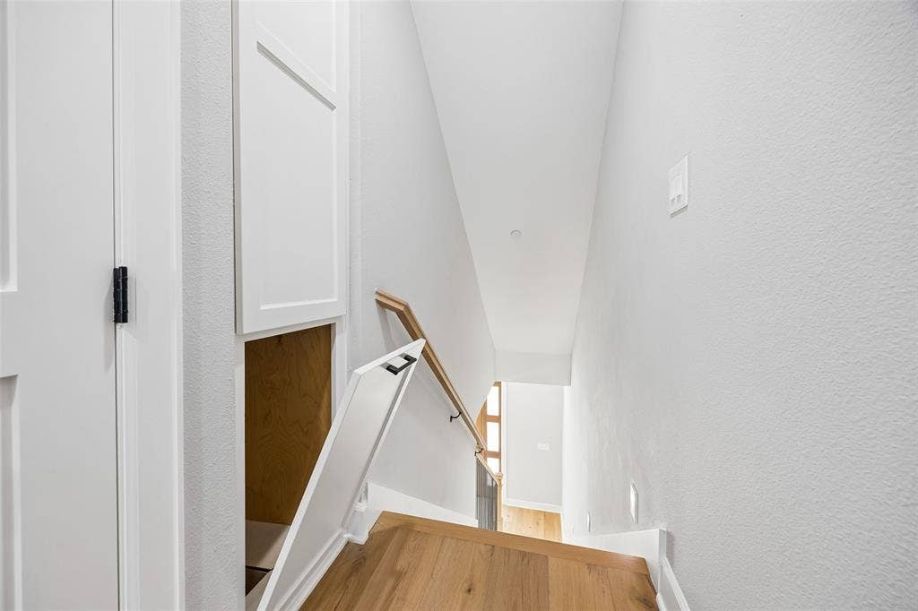 Staircase featuring wood-finish flooring, a wall-mounted wooden handrail, and built-in under-stair cabinetry with matte black hardware