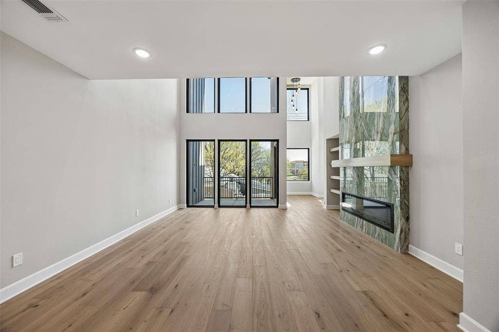 Two-story living area featuring wood-finish flooring, floor-to-ceiling stone fireplace surround with integrated hearth, built-in shelving, and expansive grid windows