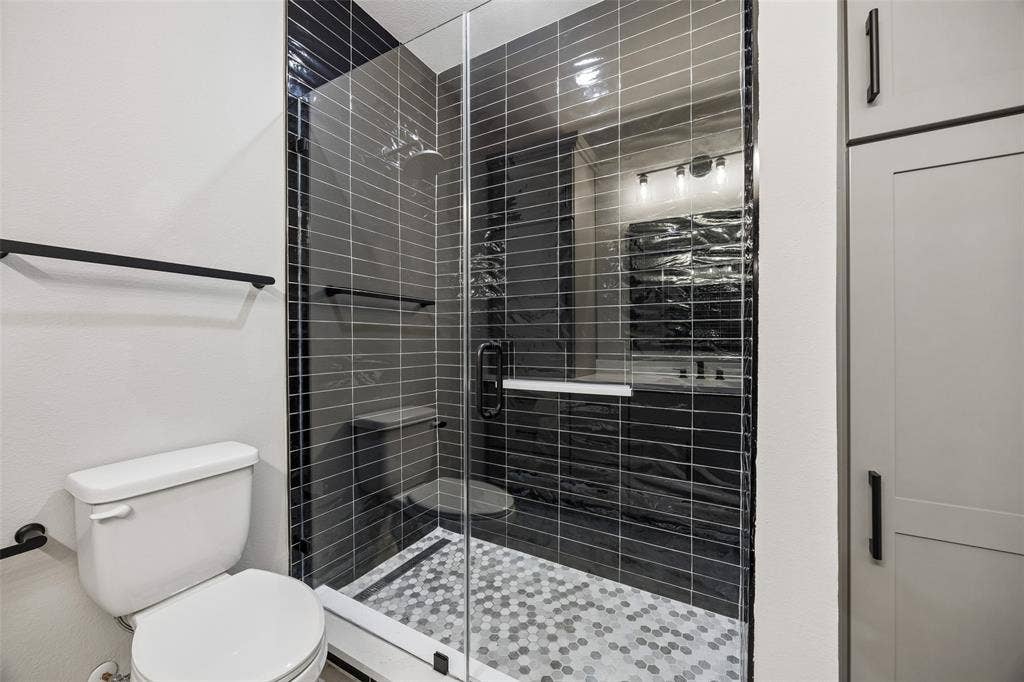 Walk-in shower featuring black subway tile surround, glass enclosure, hexagonal mosaic floor tile, and matte black hardware, accompanied by built-in floor-to-ceiling cabinetry
