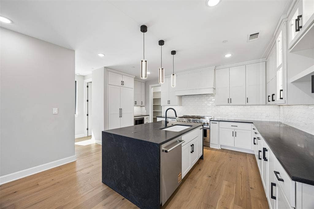 Kitchen featuring white Shaker-style cabinetry, dark stone countertops, a large center island with an undermount sink, pendant lighting, and wood-finish flooring