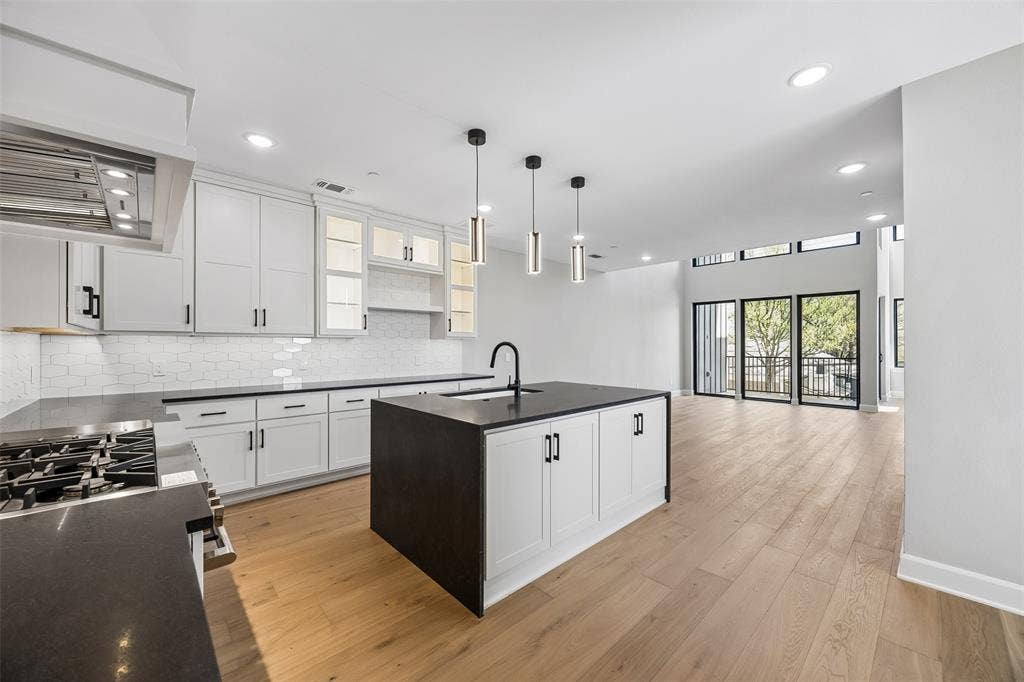 Kitchen featuring white cabinetry, dark stone countertops, an expansive center island, wood-finish flooring, and subway tile backsplash