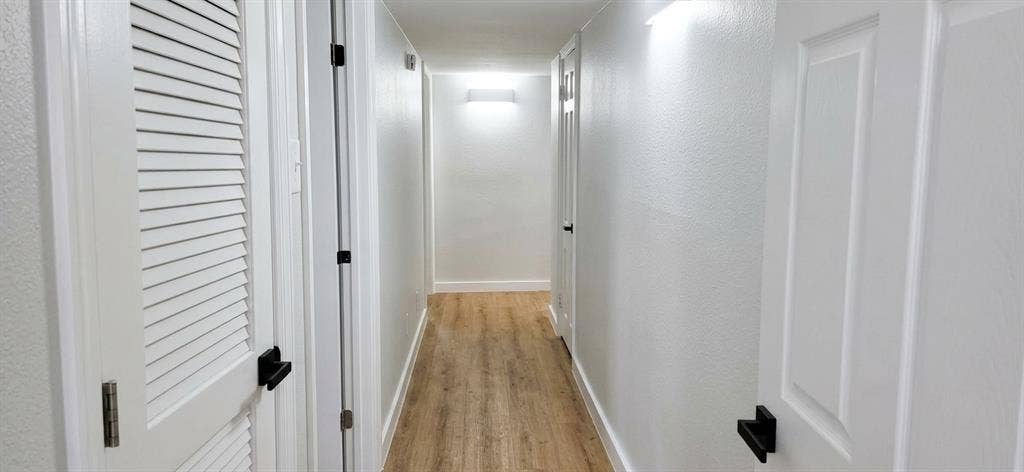 513 Vernet Street, Richardson, TX 75080 Hallway featuring wood-finish flooring, white panel doors, louvered closet door, and matte black door hardware
